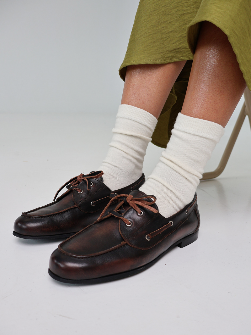 Brown leather shoes worn with white socks on a light gray background