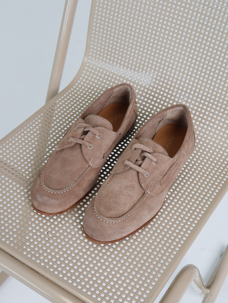 Pair of beige suede shoes on a beige chair with a white background